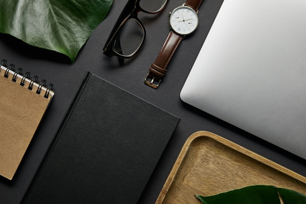 flat lay with Notebook and laptop with glasses and watch on black background